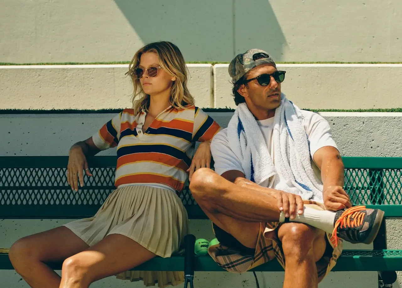Un homme et une femme portant des lunettes de soleil Garrett Leight, assis sur le banc d'un court de tennis